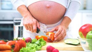 Беременная девушка режет овощи 